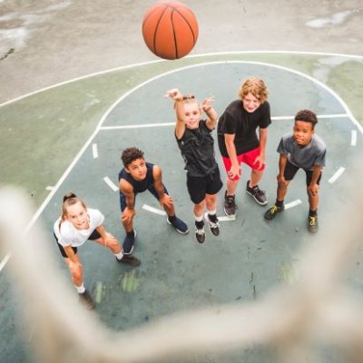A group of teenagers standing on a basketball court in anticipation as a basketball sinks into a hoop